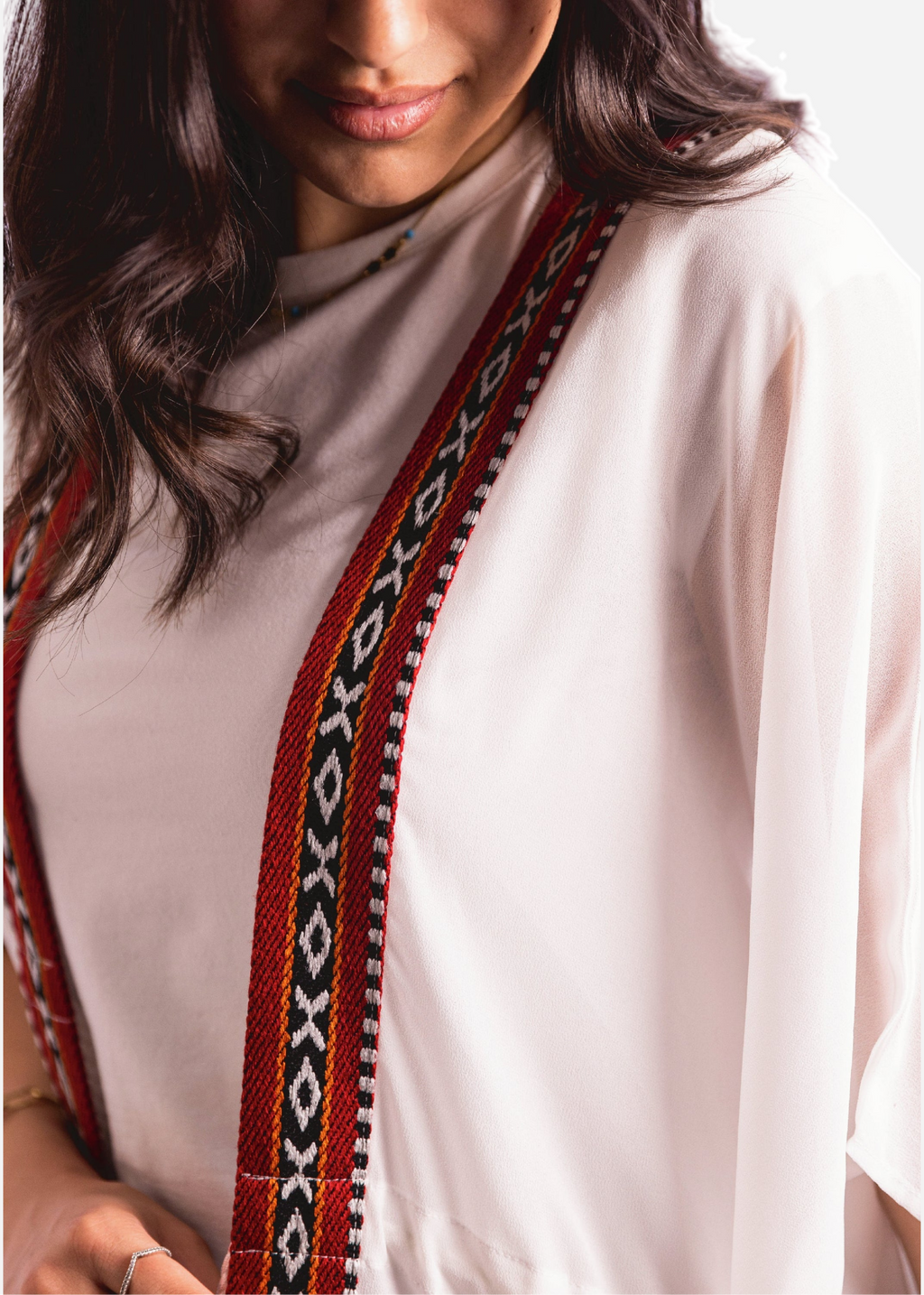 Person wearing a white top with a decorative red and black strap over the shoulder.