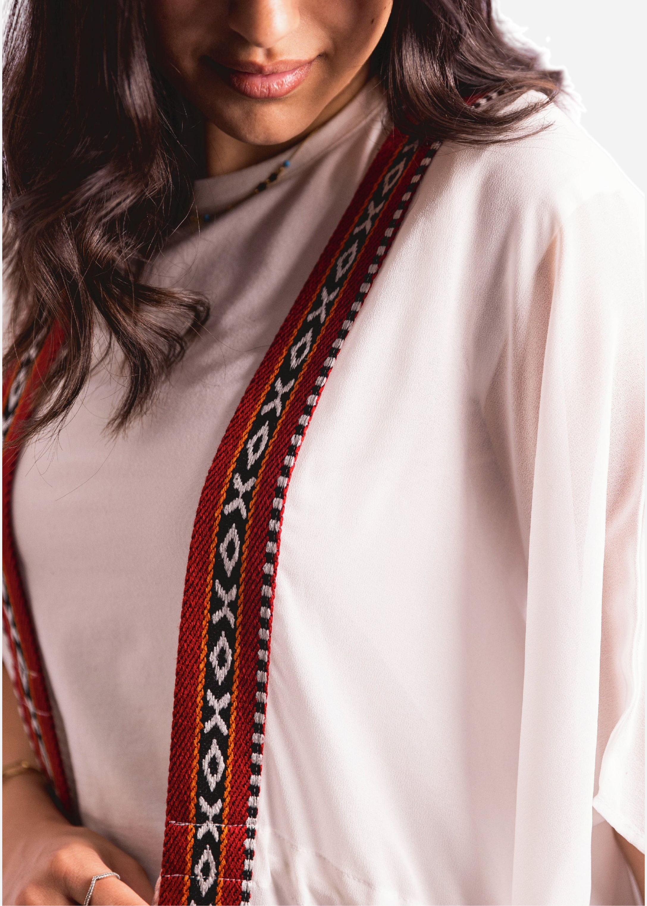 Person wearing a white top with a decorative red and black strap over the shoulder.